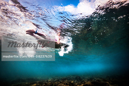 Underwater view of surfer paddling through ocean to catch waves in Bali, Indonesia