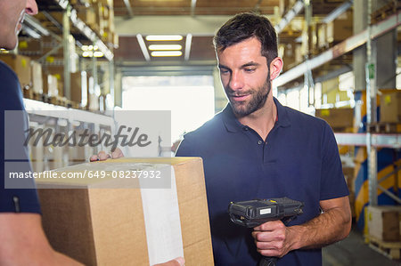 Warehouse worker using barcode scanner on cardboard box in distribution warehouse