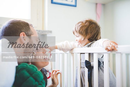 Mid adult couple laughing with toddler daughter in crib
