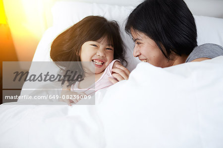 Young Chinese mother and daughter laying in bed together at home