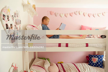 Side view of girl sitting on top bunk of bunkbed reading magazine