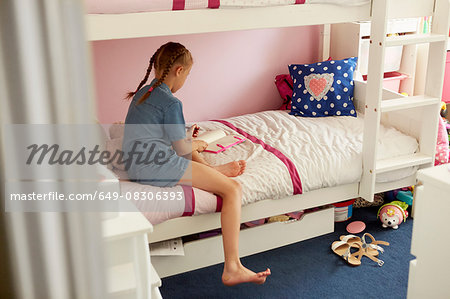Rear view of girl sitting on bunkbed writing in notebook