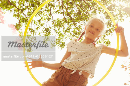 Low angle view of girl looking through hula hoop at camera smiling