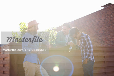 Three male friends chatting and drinking beer at rooftop party Three male friends chatting and drinking beer at rooftop party