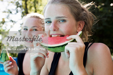 Two teenage girls eating watermelon slices in garden