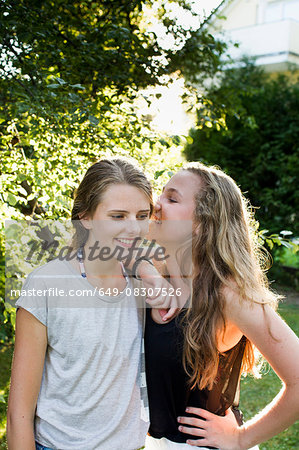 Two teenage girls whispering in garden