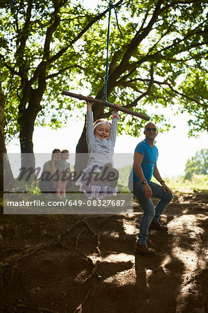 Young girl swinging on tree swing while her family watch