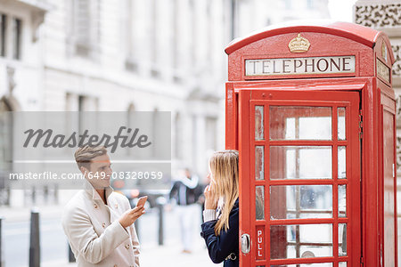 Young couple with smartphone next to red phone box, London, England, UK