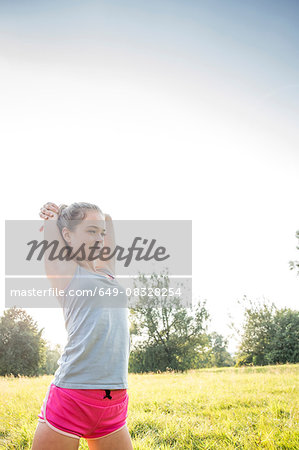 Young woman exercising, stretching, in field