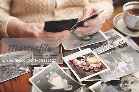 Senior woman sitting at table, looking through old photographs, mid section