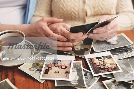 Senior woman and granddaughter sitting at table, looking through old photographs, mid section