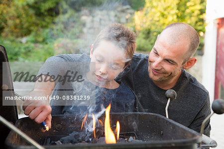 Mid adult man and son lighting barbecue in garden