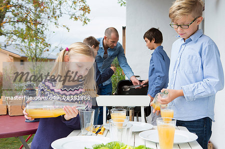 Girl and brother pouring juice at garden barbecue table