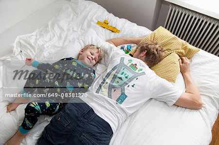 Young boy lying next to father n bed