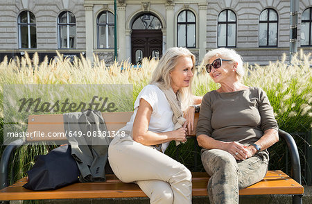 Mother and daughter sitting on bench together, outdoors