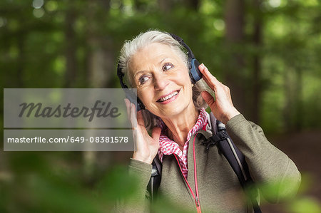 Portrait of senior woman wearing headphones, standing in forest
