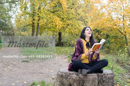 Young woman with book on tree stump, Hampstead Heath, London
