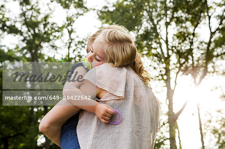Mid adult woman carrying sleeping daughter in park