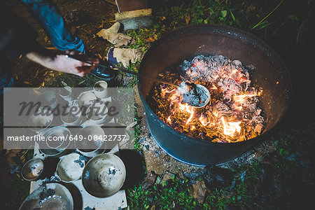 High angle view of young woman using tongs to remove clay pots from fire