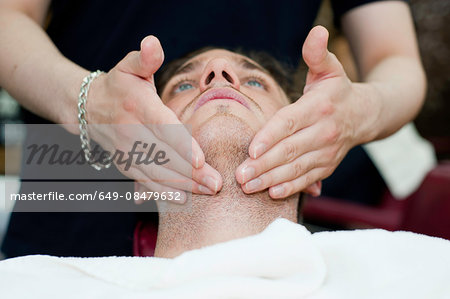 Head and shoulders of young man, head back, having facial massage