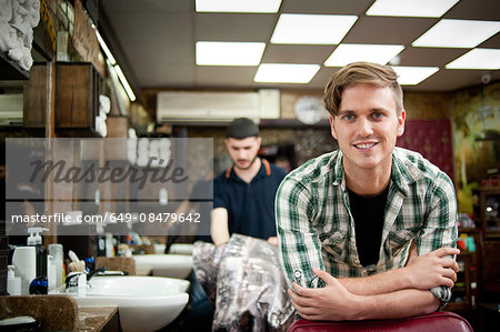 Young man in barbershop resting on elbows looking at camera smiling