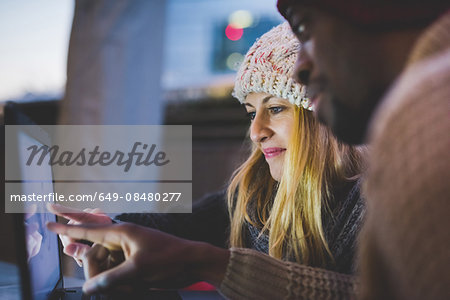 Couple using laptop outdoors at dusk