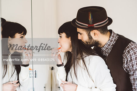 Young man with woman applying lipstick in front of mirror