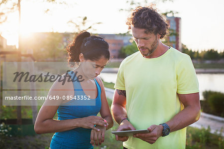 Male personal trainer and woman checking watch and digital tablet at riverside