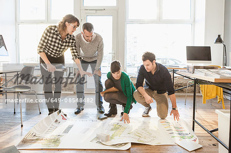 Architects discussing blueprints on wooden floor