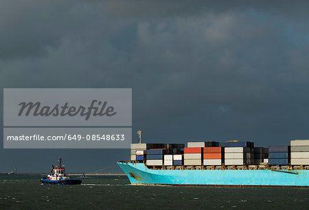 Container ship entering Rotterdam harbour with help of tug boat