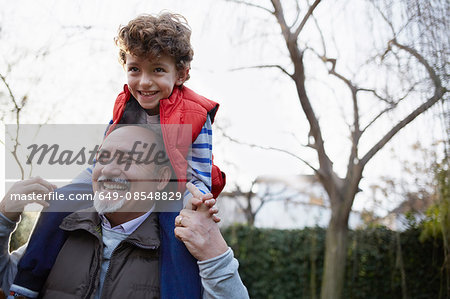 Mature man carrying grandson on shoulders smiling