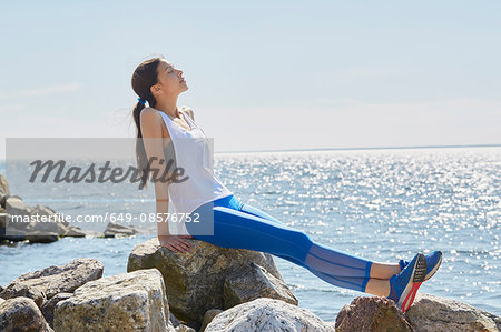 Side view of woman wearing sports clothes sitting on rocks basking in sunlight