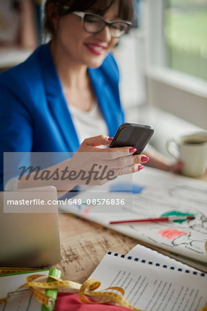 Woman in design studio sitting at desk looking at smartphone smiling