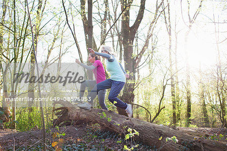 Side view of women in forest jumping over fallen tree