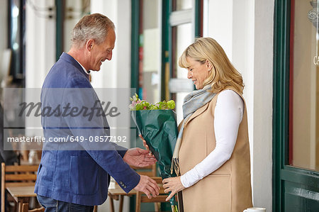 Mature man handing date bouquet at sidewalk cafe table