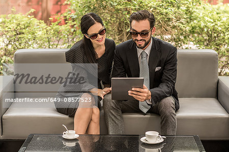 Businessman and woman reading digital tablet on hotel garden sofa, Dubai, United Arab Emirates