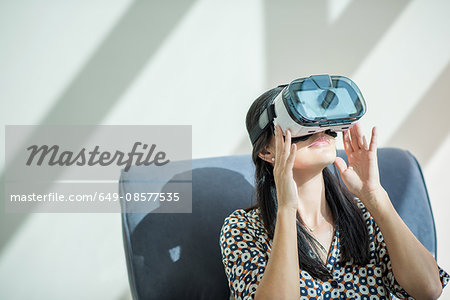 Woman on armchair looking through virtual reality headset
