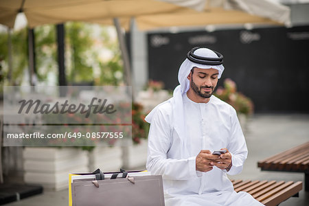 Middle eastern man wearing traditional clothes using smartphone on desert  dune, Dubai, United Arab Emirates stock photo