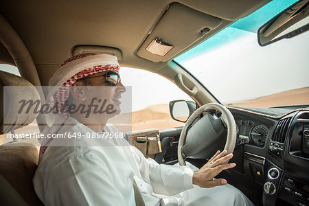 Middle eastern man wearing traditional clothes driving off road vehicle in desert, Dubai, United Arab Emirates