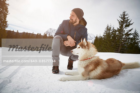 Young man crouching with husky in snow covered landscape, Elmau, Bavaria, Germany