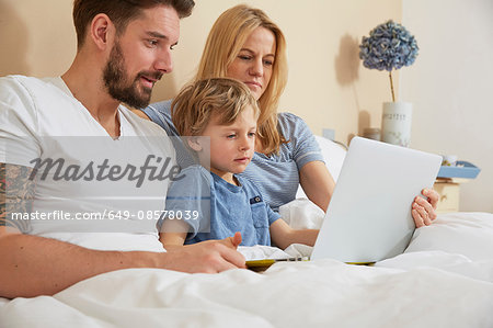 Mother and father in bed with son using digital tablet