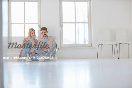Couple sitting on floor browsing digital tablet in empty new home