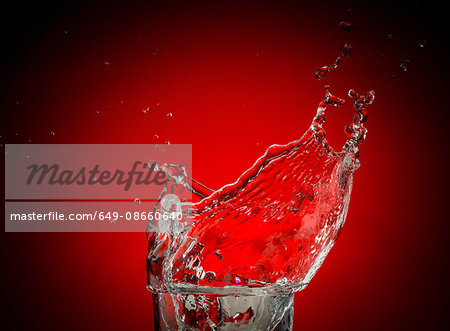 Transparent liquid and droplets splashing against red background Transparent liquid and droplets splashing against red background