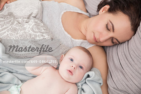 Mother lying on bed with baby boy, overhead view