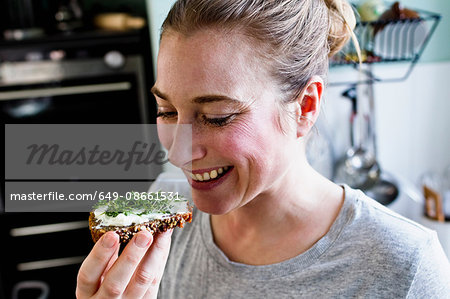 Mid adult woman eating rye bread snack in kitchen Mid adult woman eating rye bread snack in kitchen