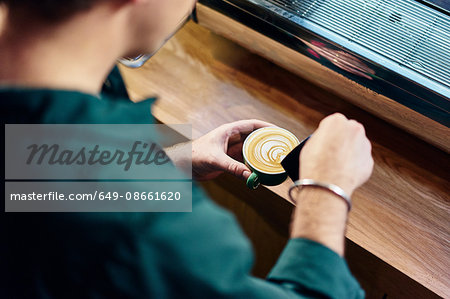 Over shoulder view of male barista pouring milk into cup in coffee shop