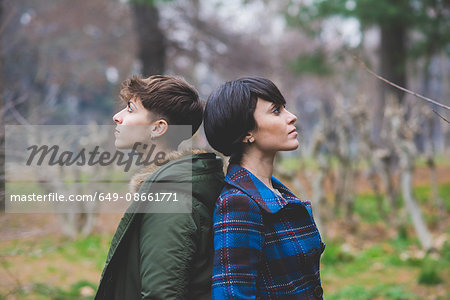 Two young women standing back to back in rural setting