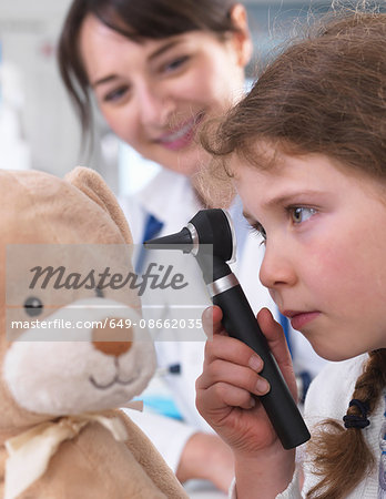 Girl using otoscope to examine teddy bear