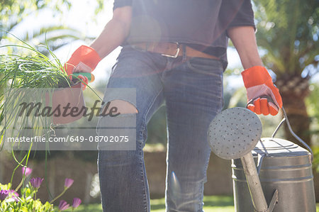 Woman carrying plant and watering can in garden