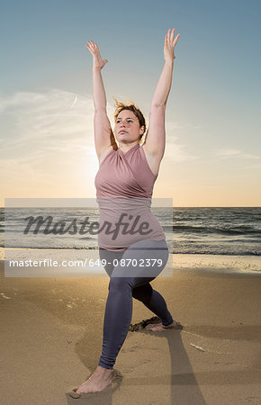 Mature woman practising yoga on a beach at sunset, warrior pose